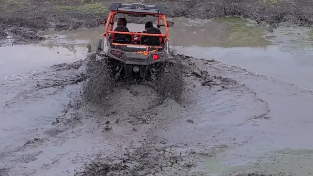 Orange Polaris RZR splashing through mud and water at 281 Country Club TX